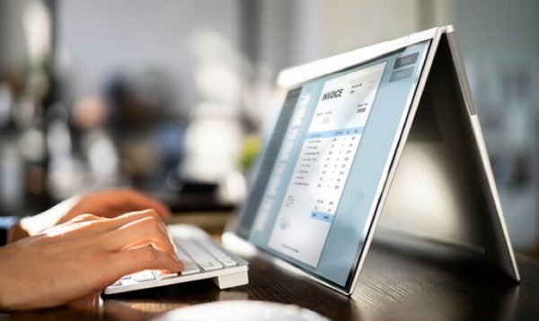 Persona utilizando un software de factura electrónica en un ordenador portátil convertible, optimizando la gestión de facturas digitales.